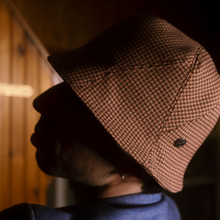 Julio is wearing a Le Panache Paris© bucket hat made in France with Go Couture_64183, Gabriel© brand fabric, 100% Trevira cs, brown houndstooth pattern on a pink background.